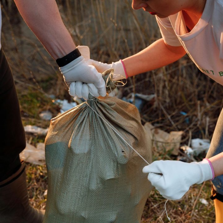 Two people tying a sack of garbage during an outdoor community cleanup activity.